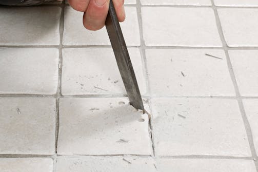 Fres ut fugene rundt en ødelagt flis med multikutter: Bank forsiktig hull med hammer og meisel, så flisen kan fjernes bit for bit. Fres ut fugene rundt en ødelagt flis med multikutter: Bank forsiktig hull med hammer og meisel, så flisen kan fjernes bit for bit.